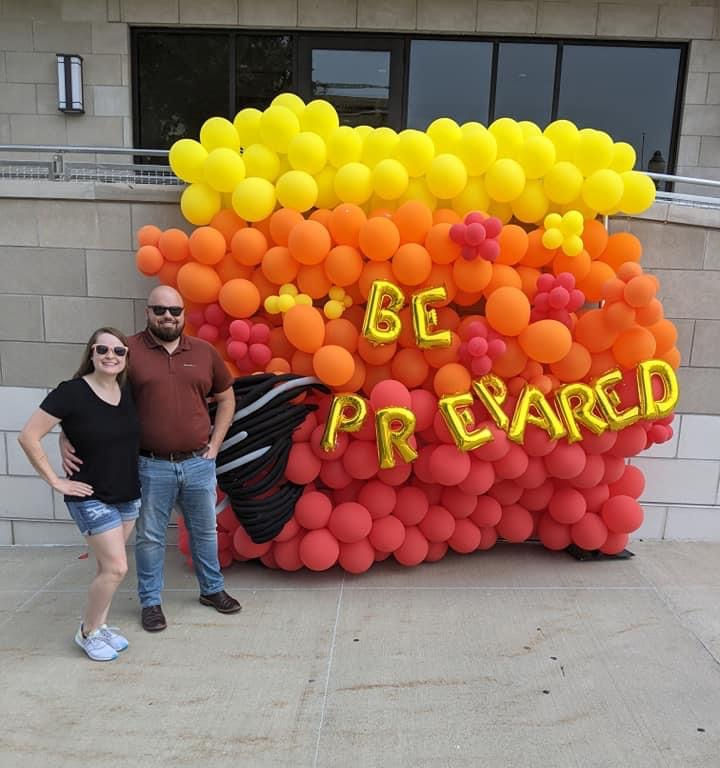 Nick and Taylor Knoth pose for a photo in front of the Be Prepared balloon wall before visiting the OEM booth.